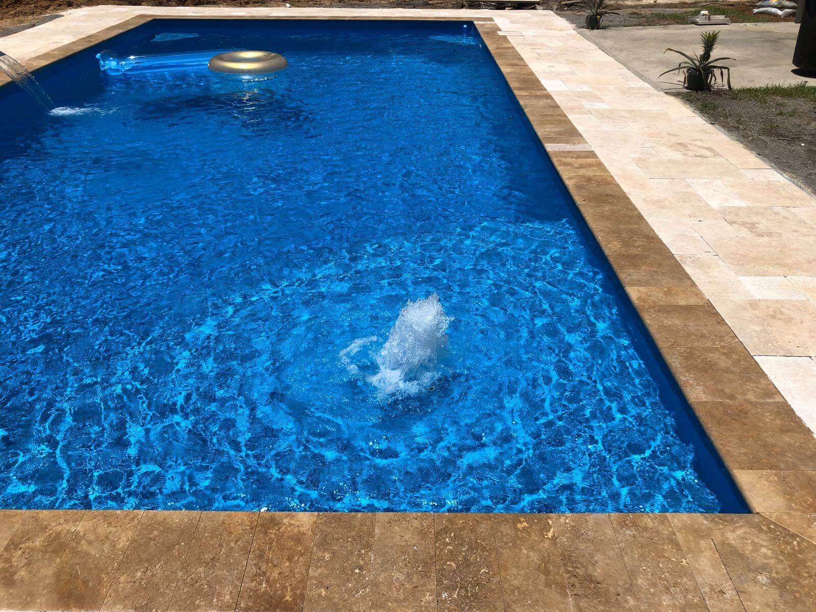 Rectangular fiberglass pool with travertine coping installed by Maxima Pools