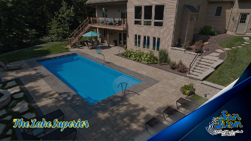 Lake Superior rectangle pool with a tan patio and a big house in background